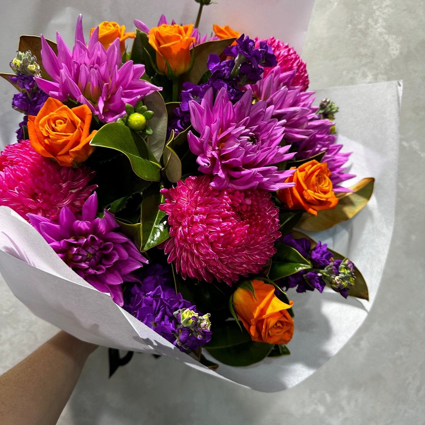 The Aperol Spritz Gift Pack by FlowersonNortonSt is a summer-inspired bouquet featuring pink and purple flowers with small orange roses, elegantly wrapped in white paper. This arrangement is as delightful as a glass of Prosecco, set against a neutral background.