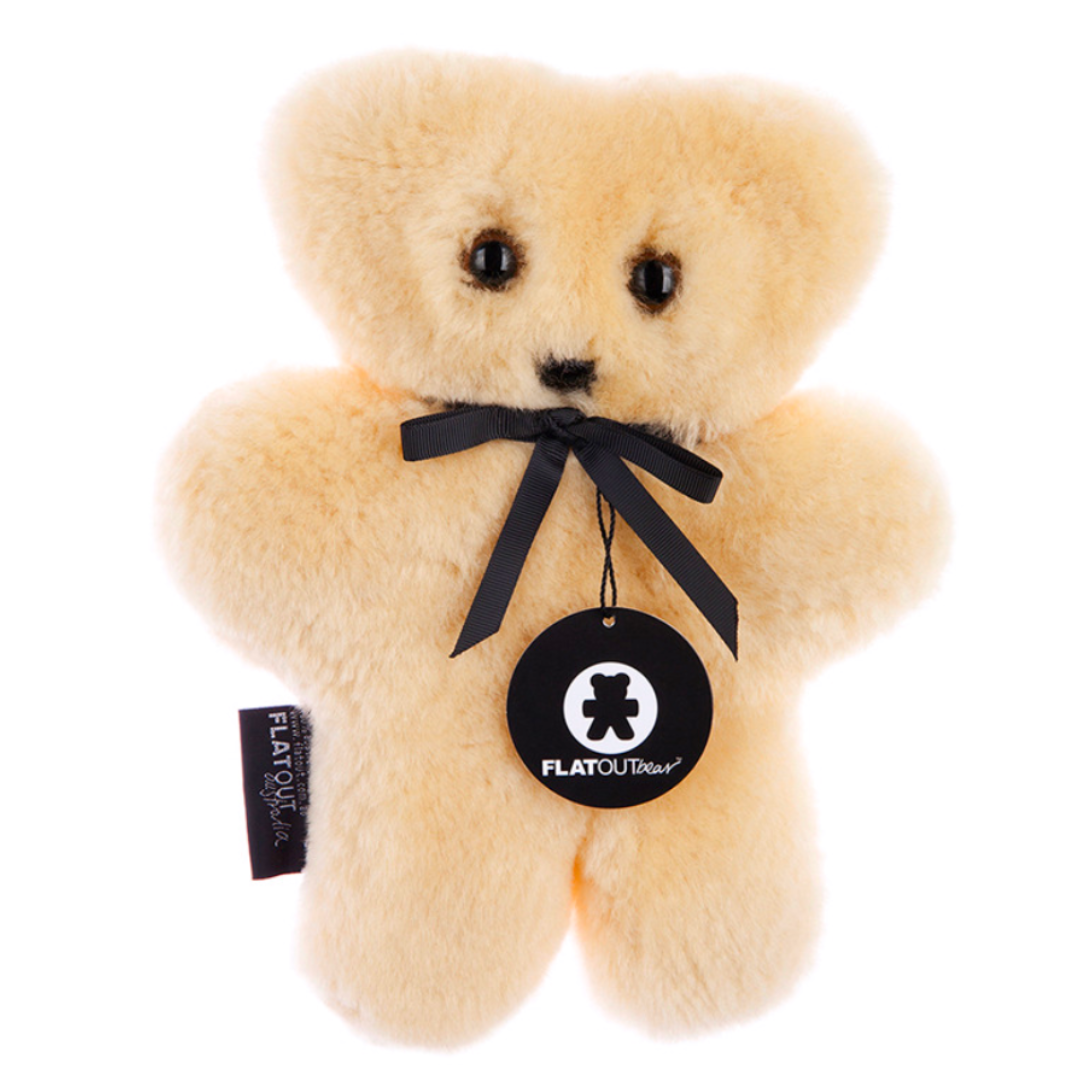 The Flatout Bears Baby Toy by Flowers on Norton St is a comforting cream-colored teddy bear with a black ribbon bow, round nose, and dark eyes. It includes a logo tag on the ribbon and an Australian sheepskin label stitched to its side.