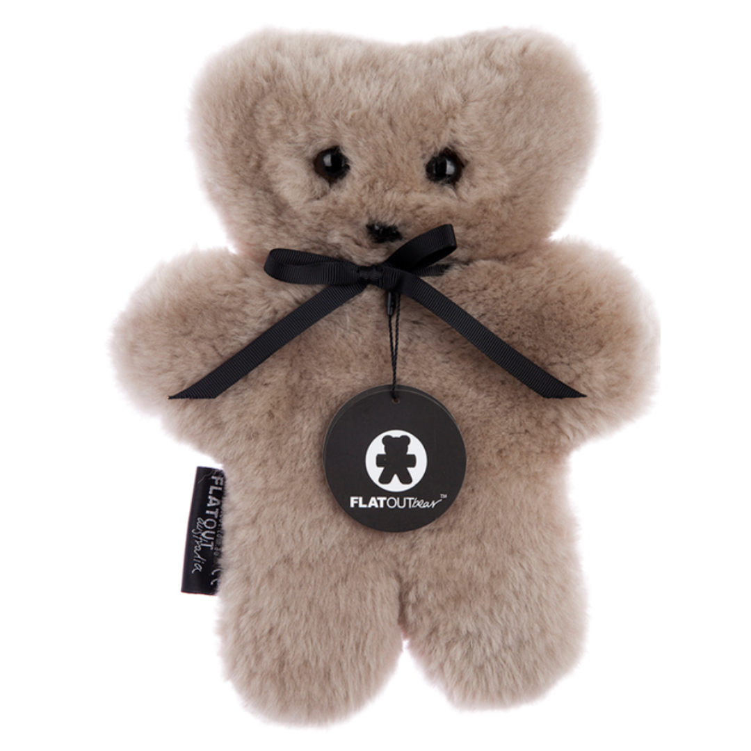 The Flatout Bears Baby Toy by Flowers on Norton St is a plush, light brown bear made from Australian sheepskin. It features a black ribbon around its neck, a round tag that reads "FLATOUTbear," and small black button eyes, offering a soft, fluffy texture for comfort.