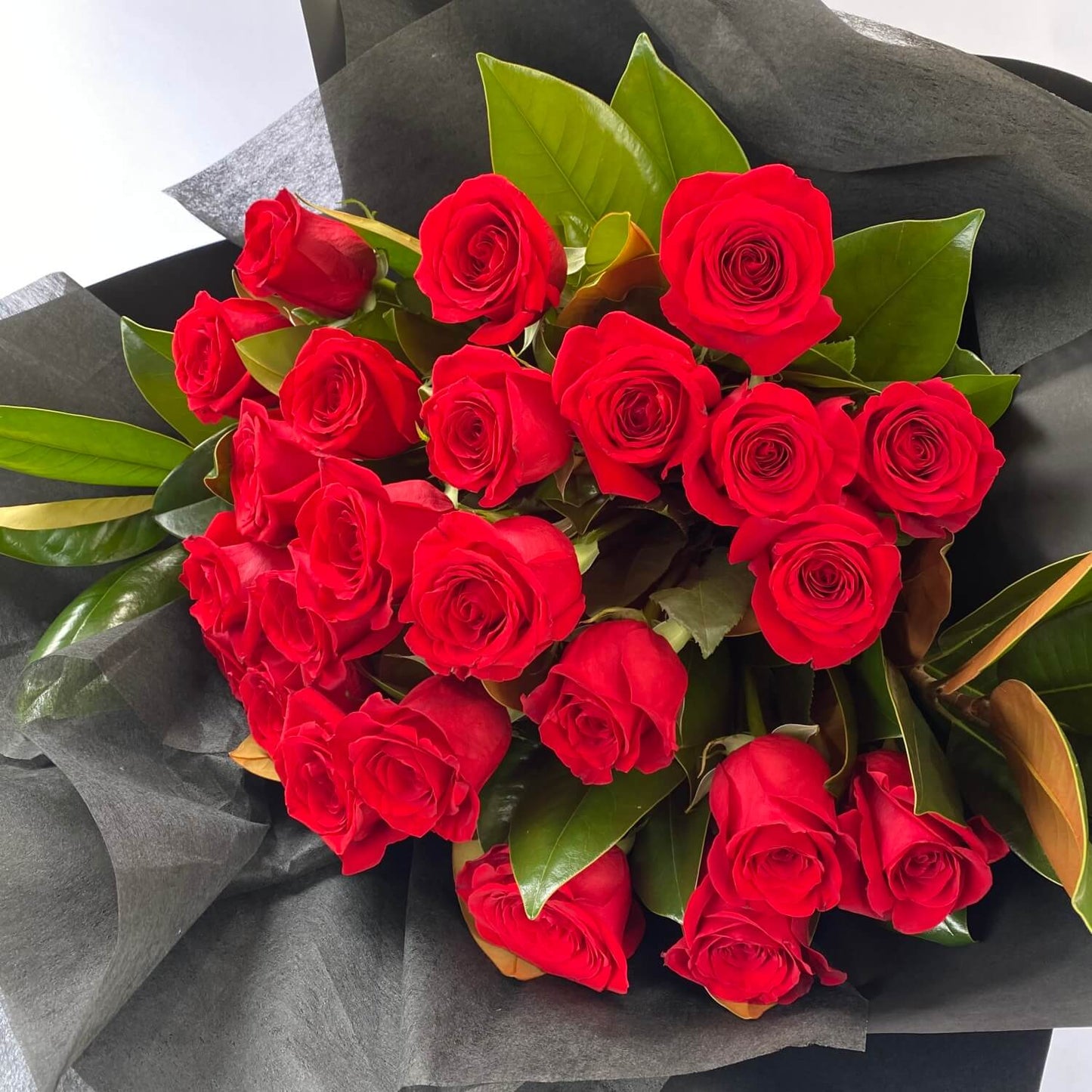 The Red Rose Bouquet 2024 by Flowers on Norton St features vibrant Colombian red roses with tightly closed petals, surrounded by dark green leaves and elegantly wrapped in black paper. It's perfect for a romantic occasion, creating a striking contrast against the dark wrap.