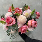 The Pretty in Pink Mixed Flowers bouquet from Flowers on Norton St showcases a luxurious arrangement against a gray background, featuring vibrant pink roses, light pink dahlias, creamy pom-pom chrysanthemums, and green eucalyptus leaves. The harmonious blend of colors and textures creates an exquisite seasonal display.