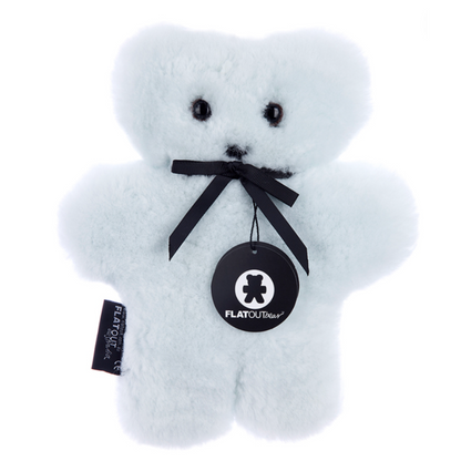 A soft, blue teddy bear crafted from Australian sheepskin features a black ribbon and a "Flatout Bear" tag around its neck. With small black eyes and nose, this comfort companion's simple design enhances its plush appearance. Product: Flatout Bears Baby Toy by Flowers on Norton St.