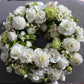 Introducing the Condolences Wreath by FlowersonNortonSt, a beautifully crafted arrangement featuring white roses, dahlias, chrysanthemums, and lush greenery elegantly displayed in a circular design on a grey background. This wreath is ideal for funeral flower arrangements and can be personalized with custom-printed ribbon messages.